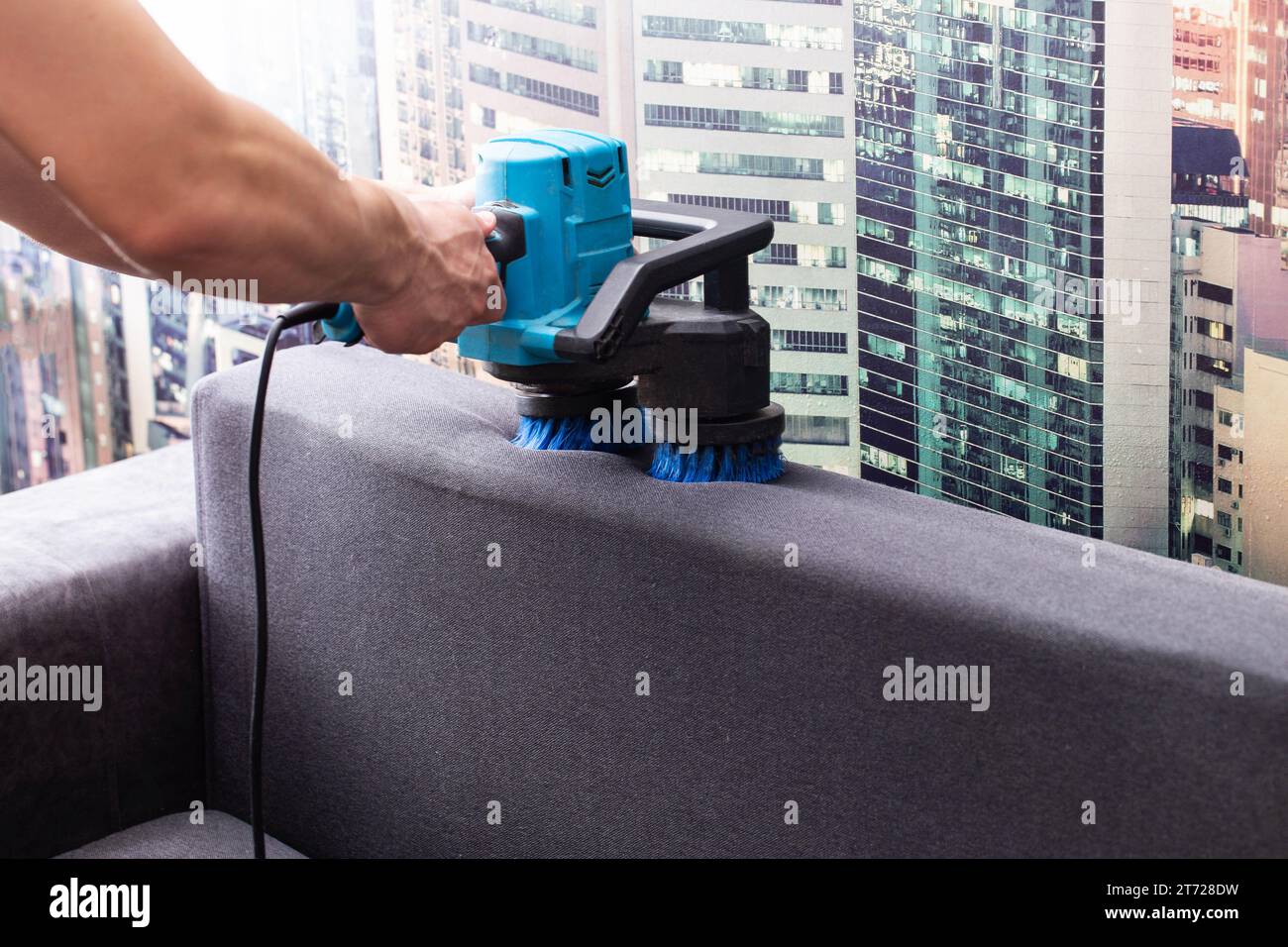 Cleaning the back of a black sofa with a special electric brush. Sofa