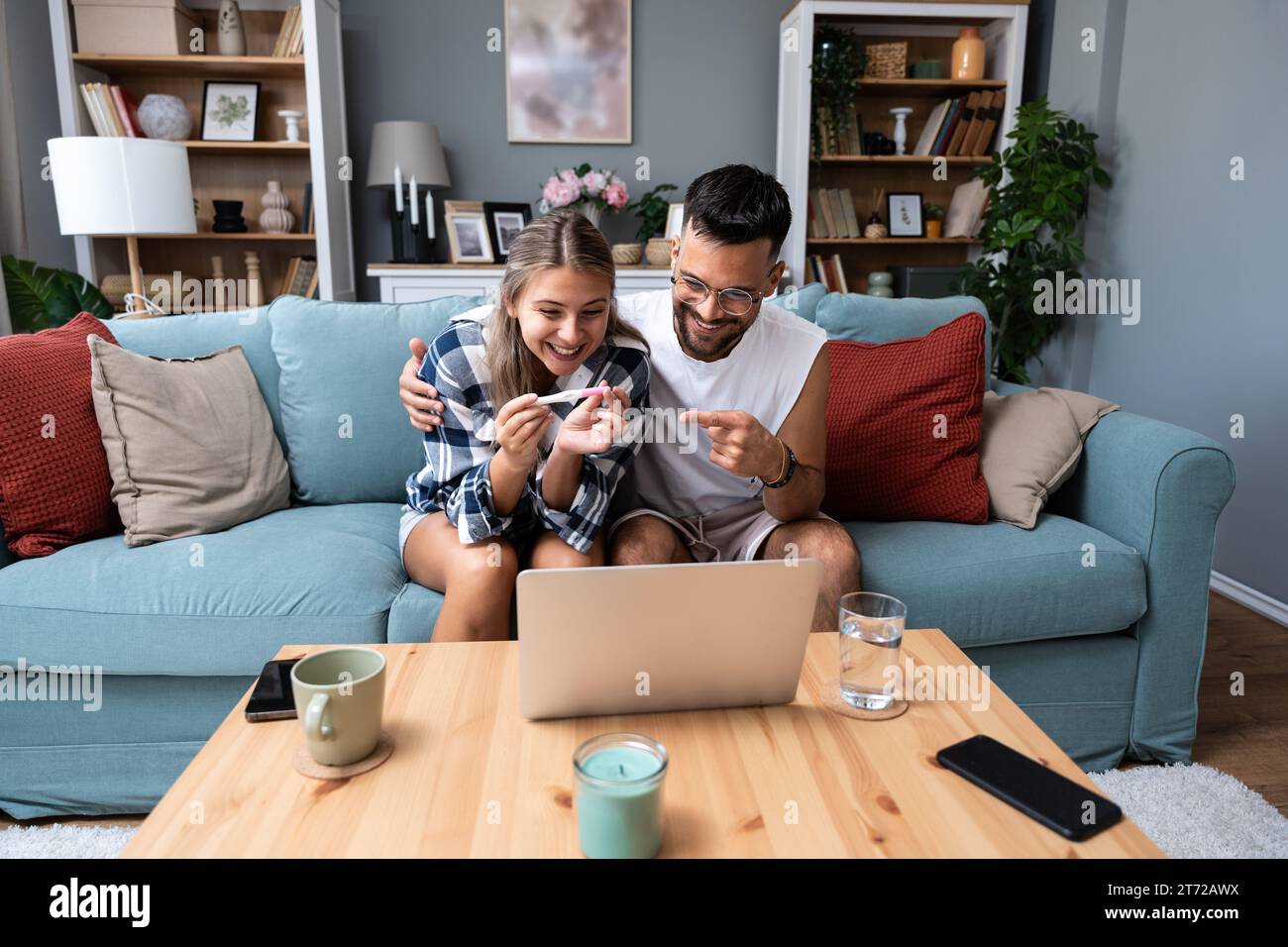 Surprised happy couple announcing their pregnancy to family and friends during a video call. Young future parents using laptop computer to share their Stock Photo