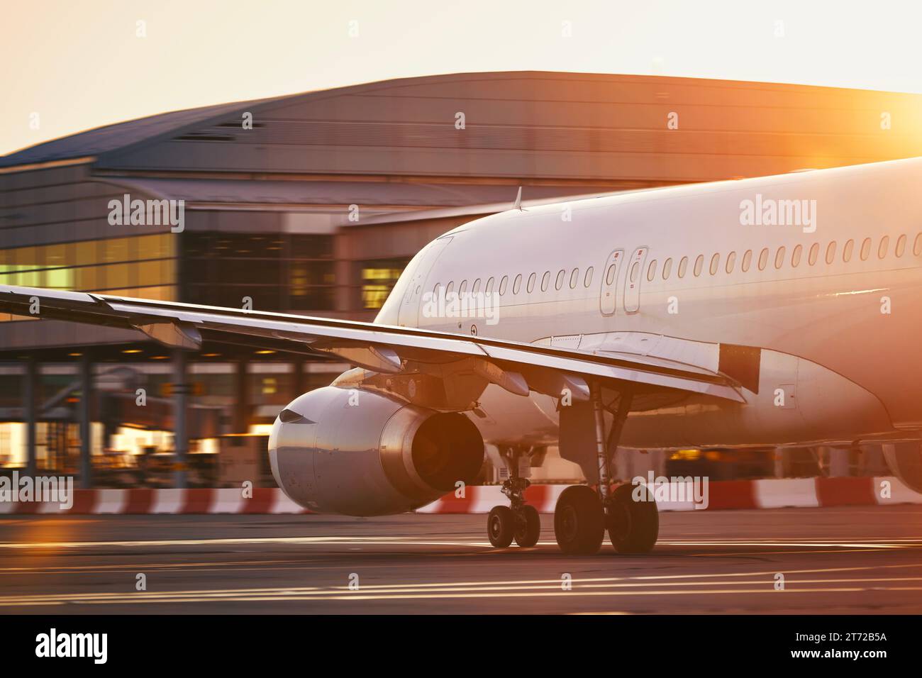 Airplane at busy airport. Passenger plane on the move against terminal building at beautiful sunrise. Stock Photo