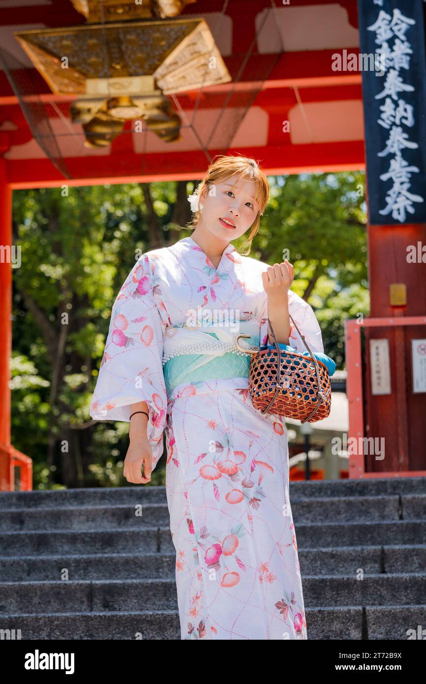 Portrait of a young woman wearing Japanese yukata summer kimono standing in front of the shrine gate. Kyoto, Japan. Stock Photo