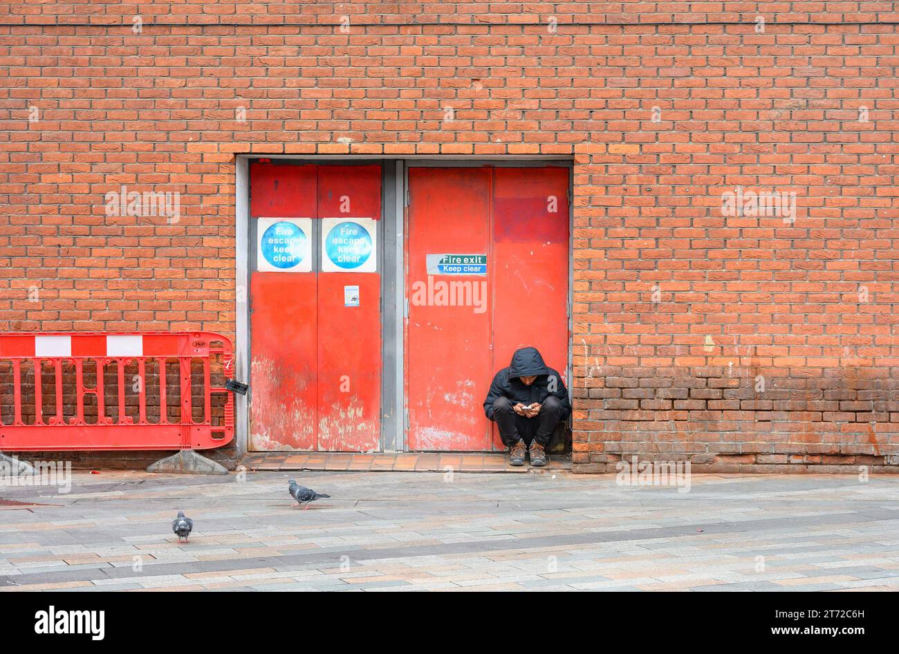 London, UK. Man sitting in a doorway in Chinatown, looking at his phone Stock Photo