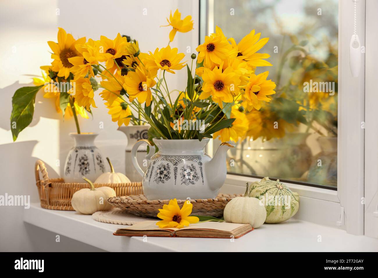 Composition with beautiful flowers, pumpkins and book on windowsill. Autumn atmosphere Stock Photo