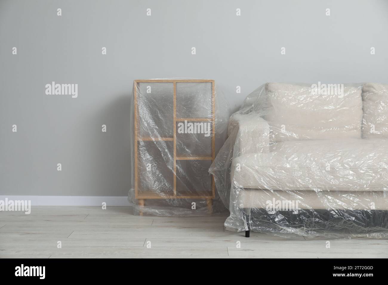 Shelving unit and sofa covered with plastic film near light grey wall indoors. Space for text Stock Photo