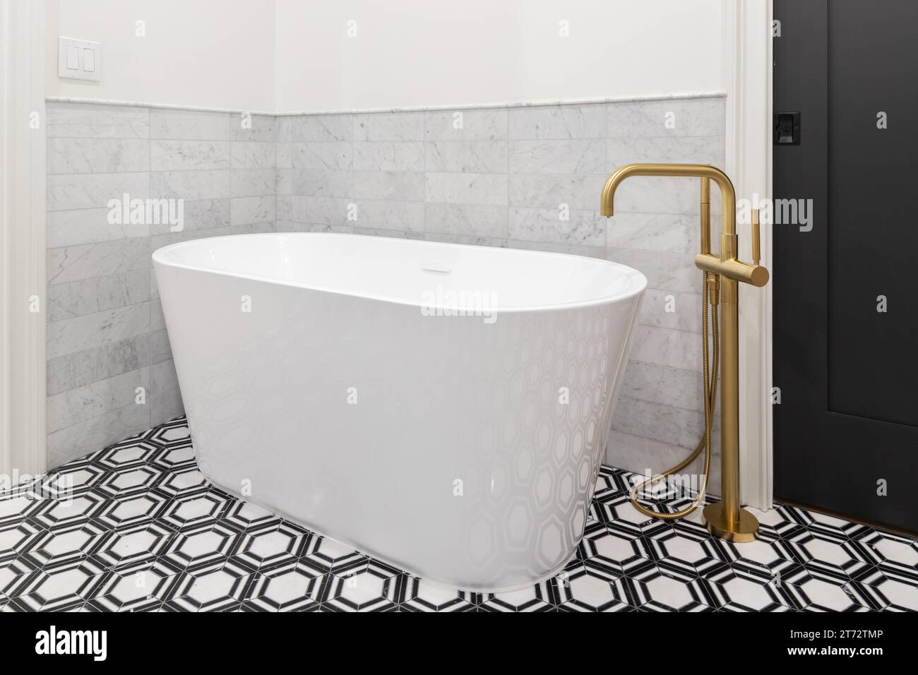 A freestanding tub with a gold faucet, black and white pattern tile