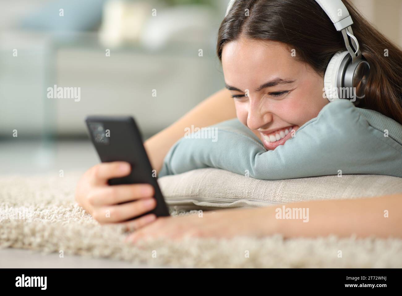 Happy woman is watching media on phone lying on the floor at home Stock Photo