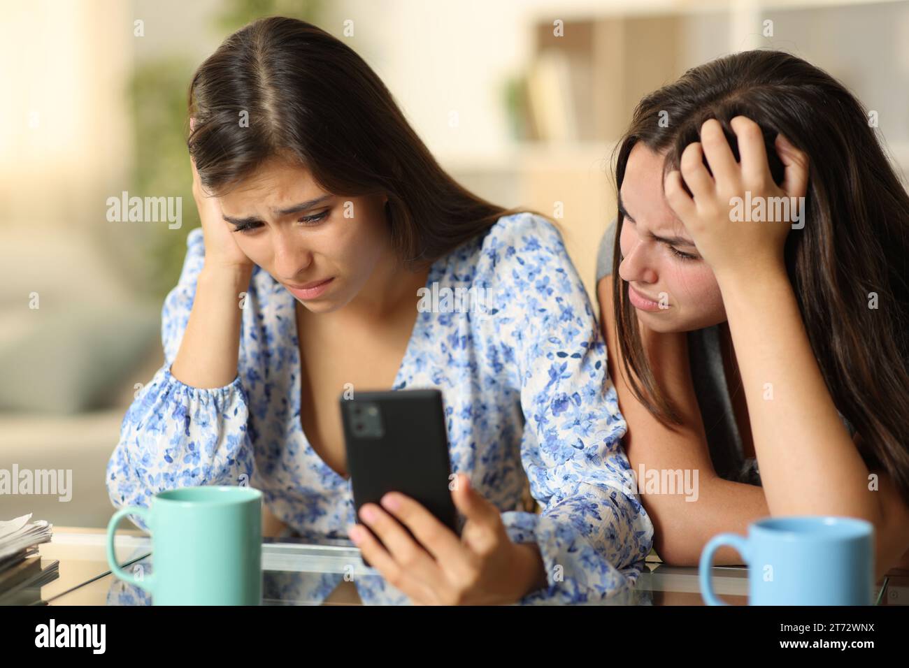 Two sad women checking bad news on cell phone at home Stock Photo
