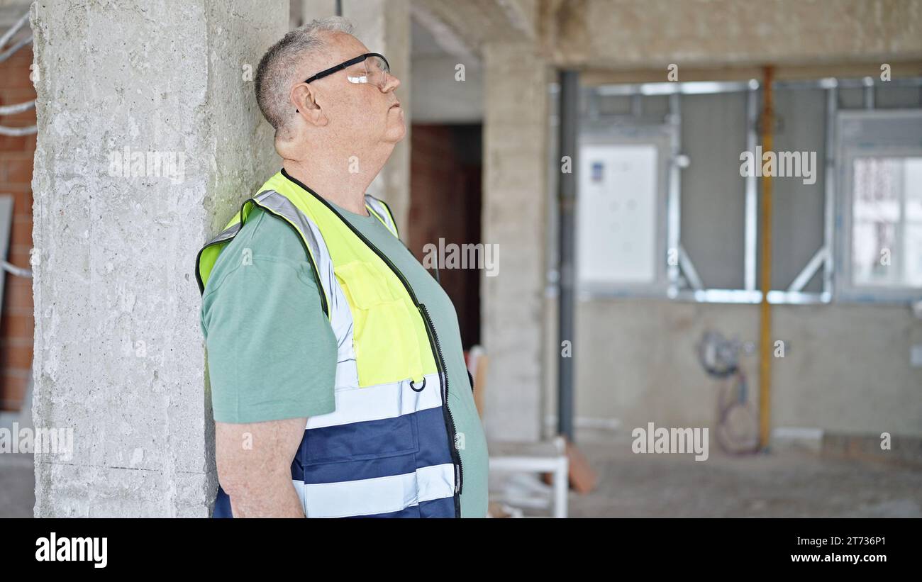Middle age grey-haired man builder leaning on wall tired at construction site Stock Photo