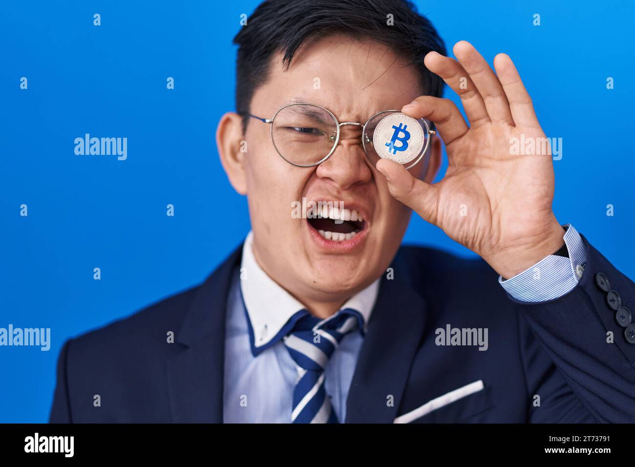 Young asian man holding virtual currency bitcoin covering eye angry and ...