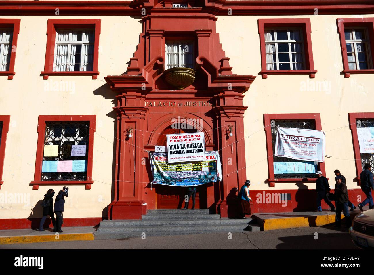 People walk past signs on the entrance of the Palacio de Justicia / Justice Palace building announcing an indefinite strike by workers, who have taken over the building. Plaza de Armas central square, Puno, Peru. The dispute was over the inclusion of justice workers in a new law for Civil Service workers (which they say threatens the autonomy of the legal system), and also changes to the pay grade system. Stock Photo
