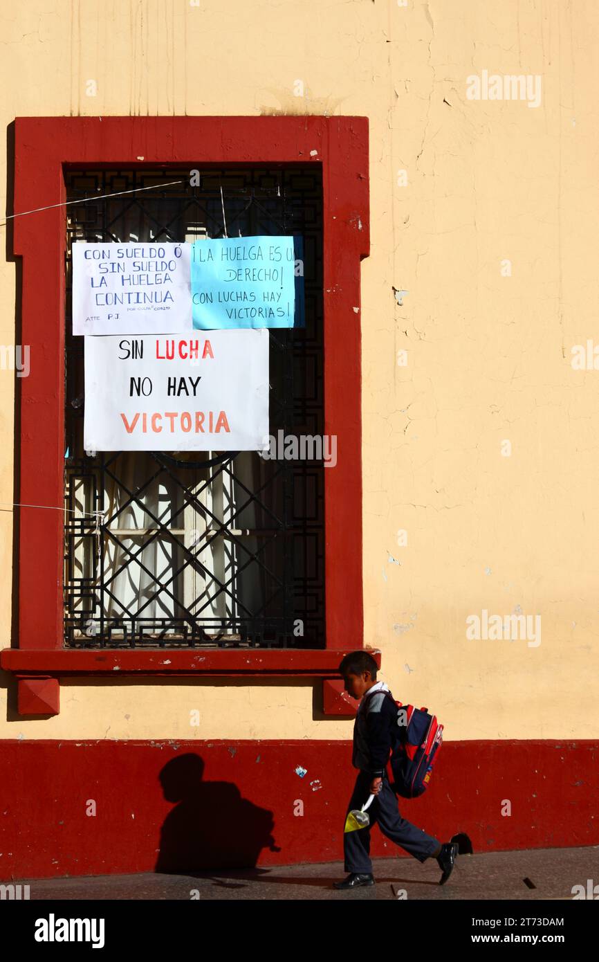 A schoolboy walks past signs on a window of the Palacio de Justicia / Justice Palace building announcing an indefinite strike by workers, who have taken over the building. Plaza de Armas central square, Puno, Peru. The dispute was over the inclusion of justice workers in a new law for Civil Service workers (which they say threatens the autonomy of the legal system), and also changes to the pay grade system. Stock Photo