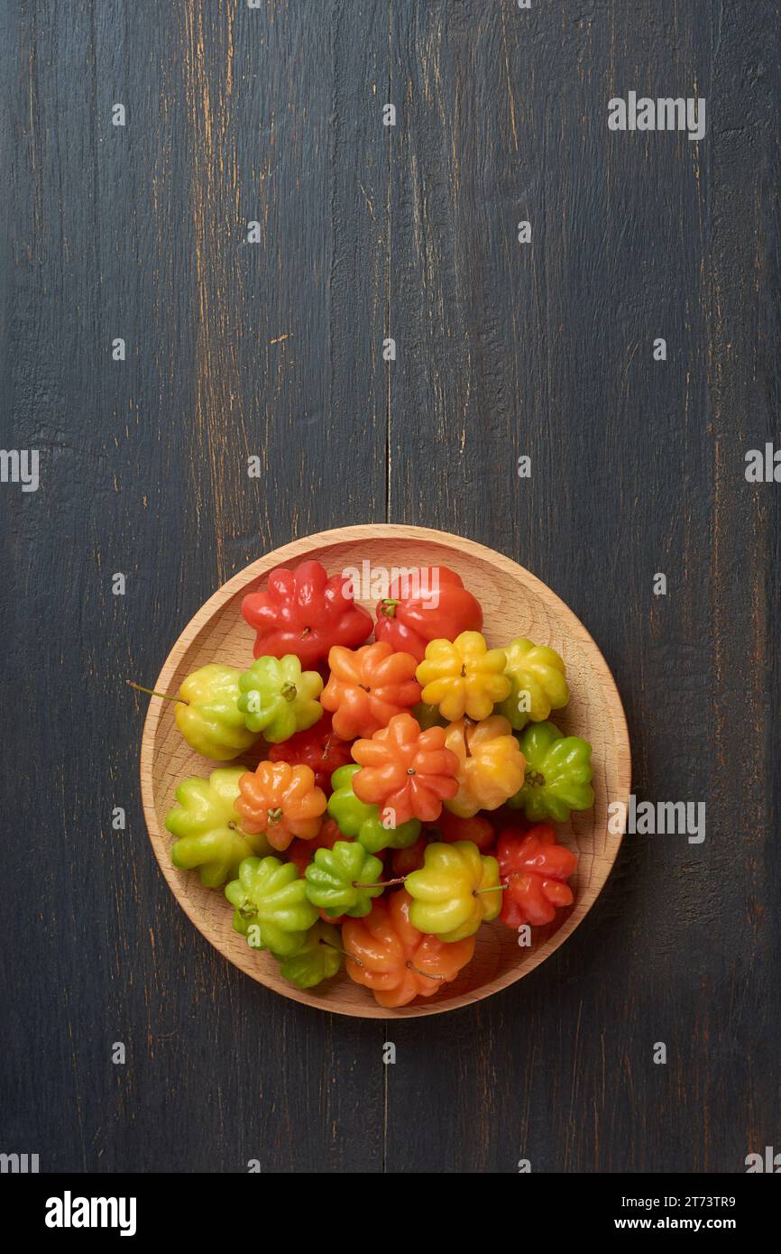 surinam cherries, eugenia uniflora, aka pitanga, brazilian or cayenne cherry, vibrant colorful fruits on wooden plate, isolated on black rustic backgr Stock Photo