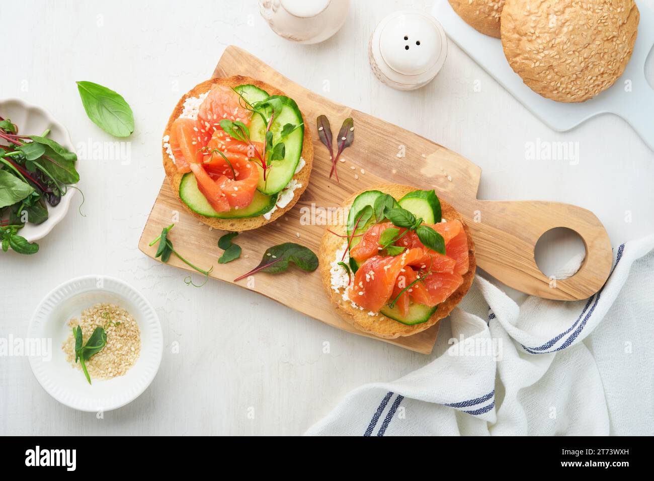 Open smoked salmon sandwiches with cream cheese, cucumber, sesame seeds, microgreens, spinach, and peas leaves on light old wooden background. Healthy Stock Photo
