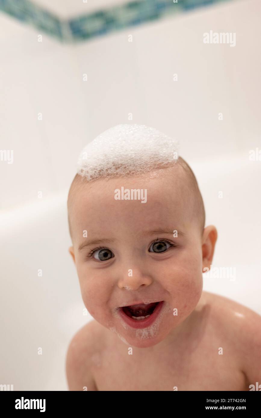 Happy, smiling baby in a bath with soap bubbles on his head and white