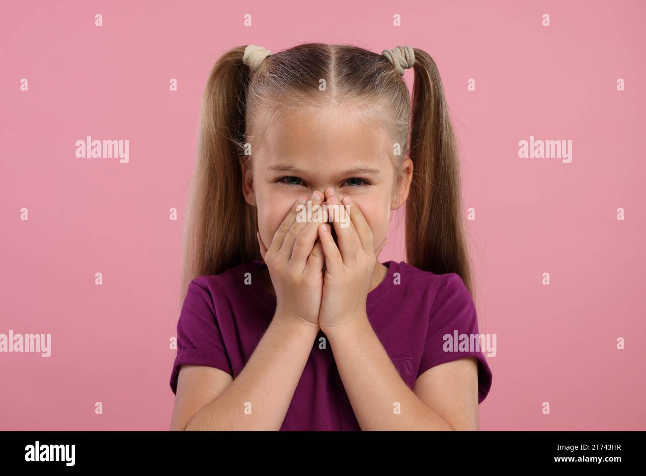 Embarrassed little girl covering her mouth with hands on pink background Stock Photo