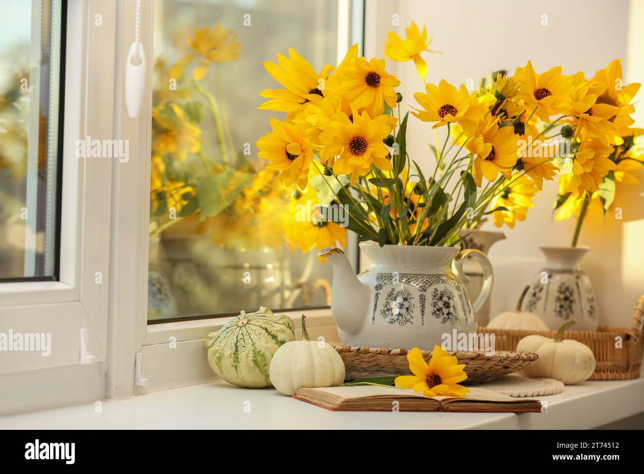 Composition with beautiful flowers, pumpkins and book on windowsill. Autumn atmosphere Stock Photo
