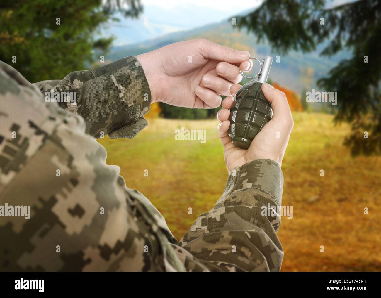 Soldier pulling safety pin out of hand grenade outdoors, closeup Stock