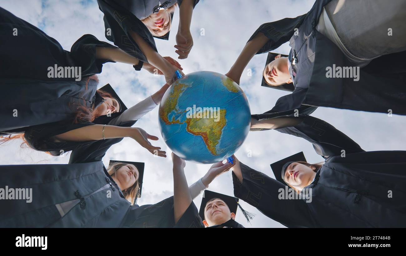 Graduating students spin a geographical globe of the world. Stock Photo