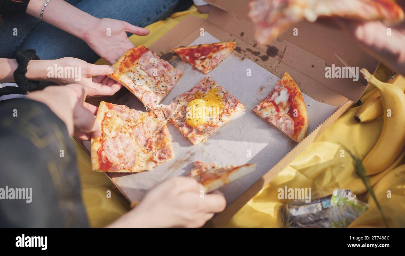 Young students' hands reach for the pizza. Stock Photo