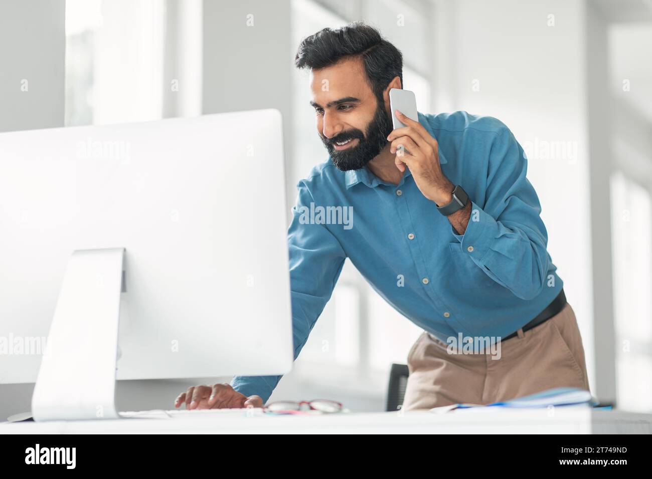 Smiling indian man talking on phone using computer Stock Photo