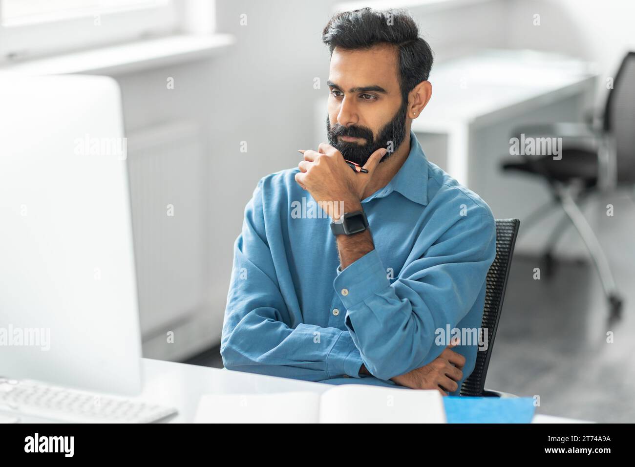 Thoughtful indian man with beard looking at computer Stock Photo