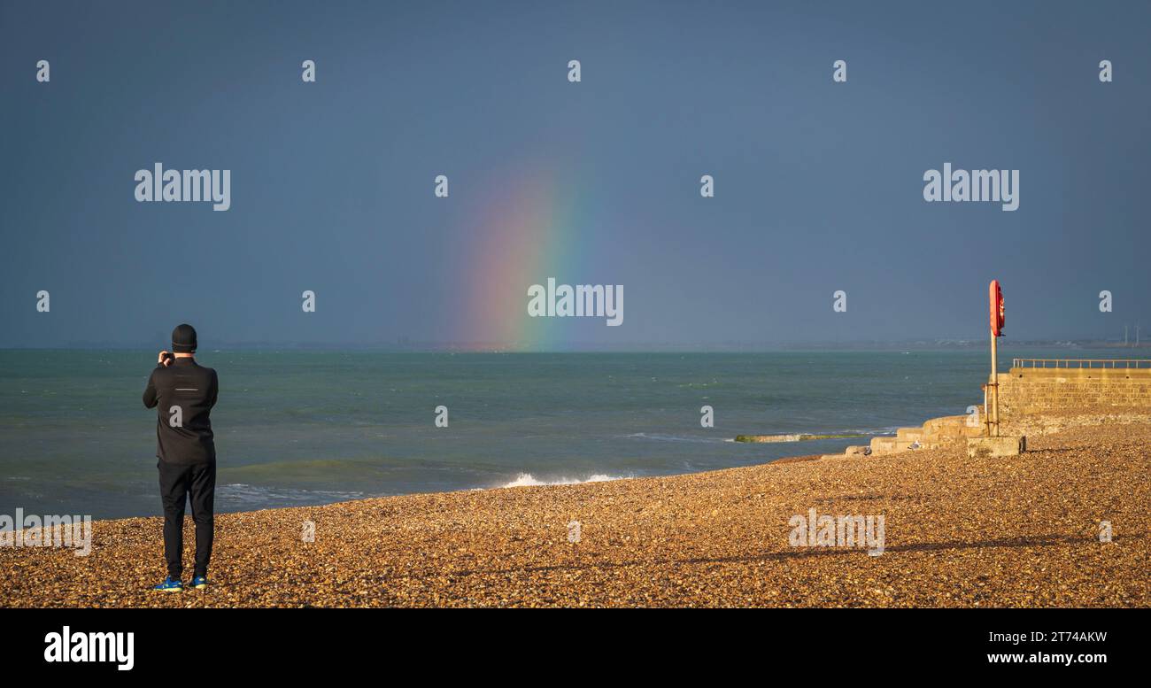 Somebody taking pictures of a rainbow on the seafront in the early morning as the rain sweeps in. Brighton, Sussex, England, UK Stock Photo