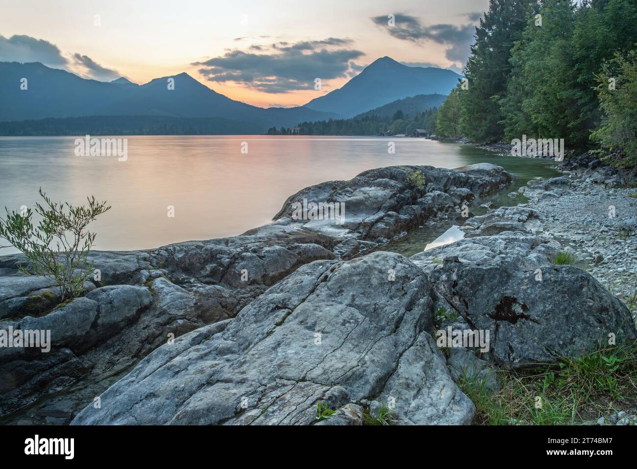 A scenic lake surrounded by majestic mountains, lush green grass, and ...