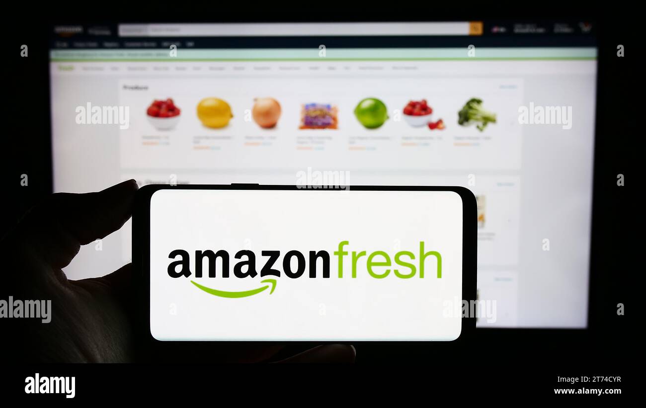 Person holding cellphone with logo of US grocery retail company Amazon Fresh in front of business webpage. Focus on phone display. Stock Photo