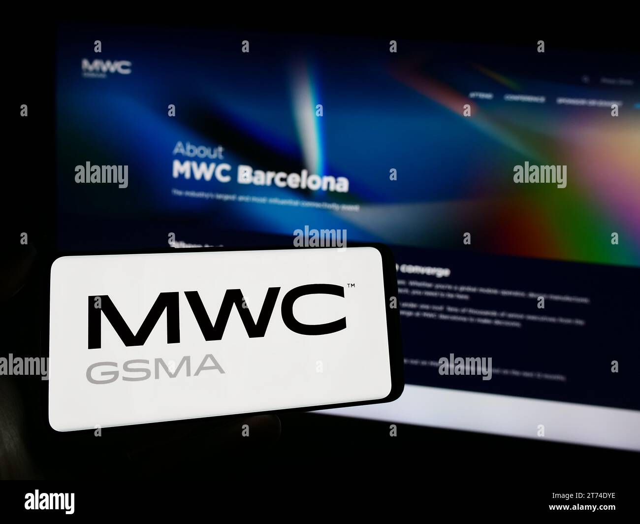 Person holding smartphone with logo of annual mobile communications trade show MWC Barcelona in front of website. Focus on phone display. Stock Photo