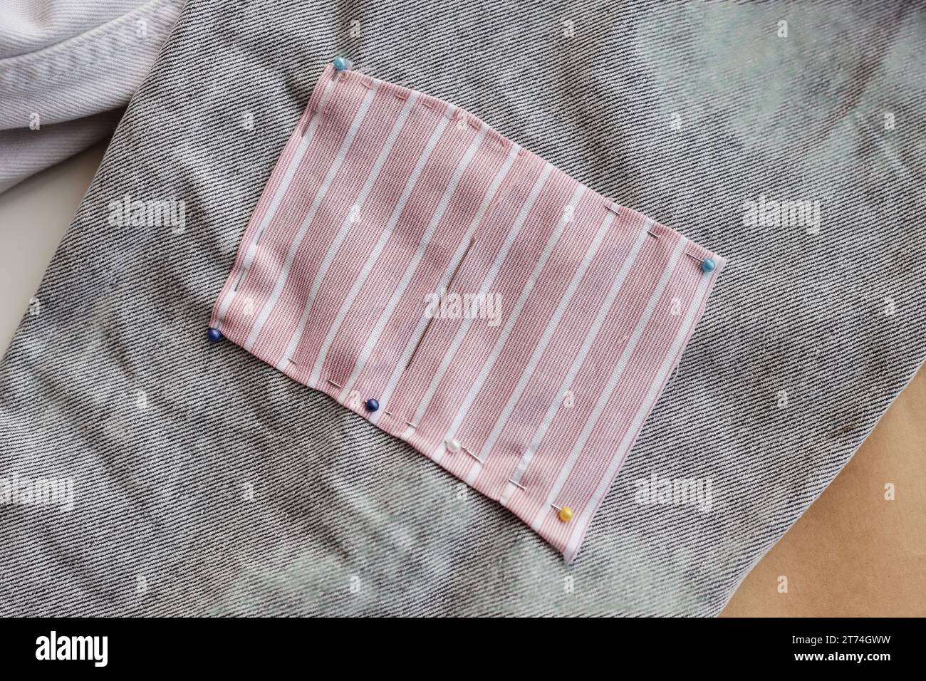 Rectangular piece of striped fabric pinned to grey jeans during upcycling or customization process in studio of slow fashion or stylist workshop Stock Photo