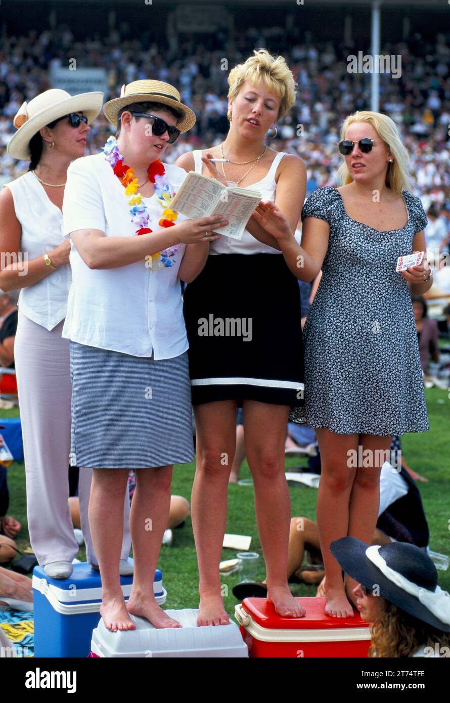 Group of young women standing on picnic boxes to get a better view of the horse racing. They are studying the race card and hoping for the best. Royal Ascot horse racing.  Ascot, Berkshire, England circa June  2005 2000s UK HOMER SYKES Stock Photo
