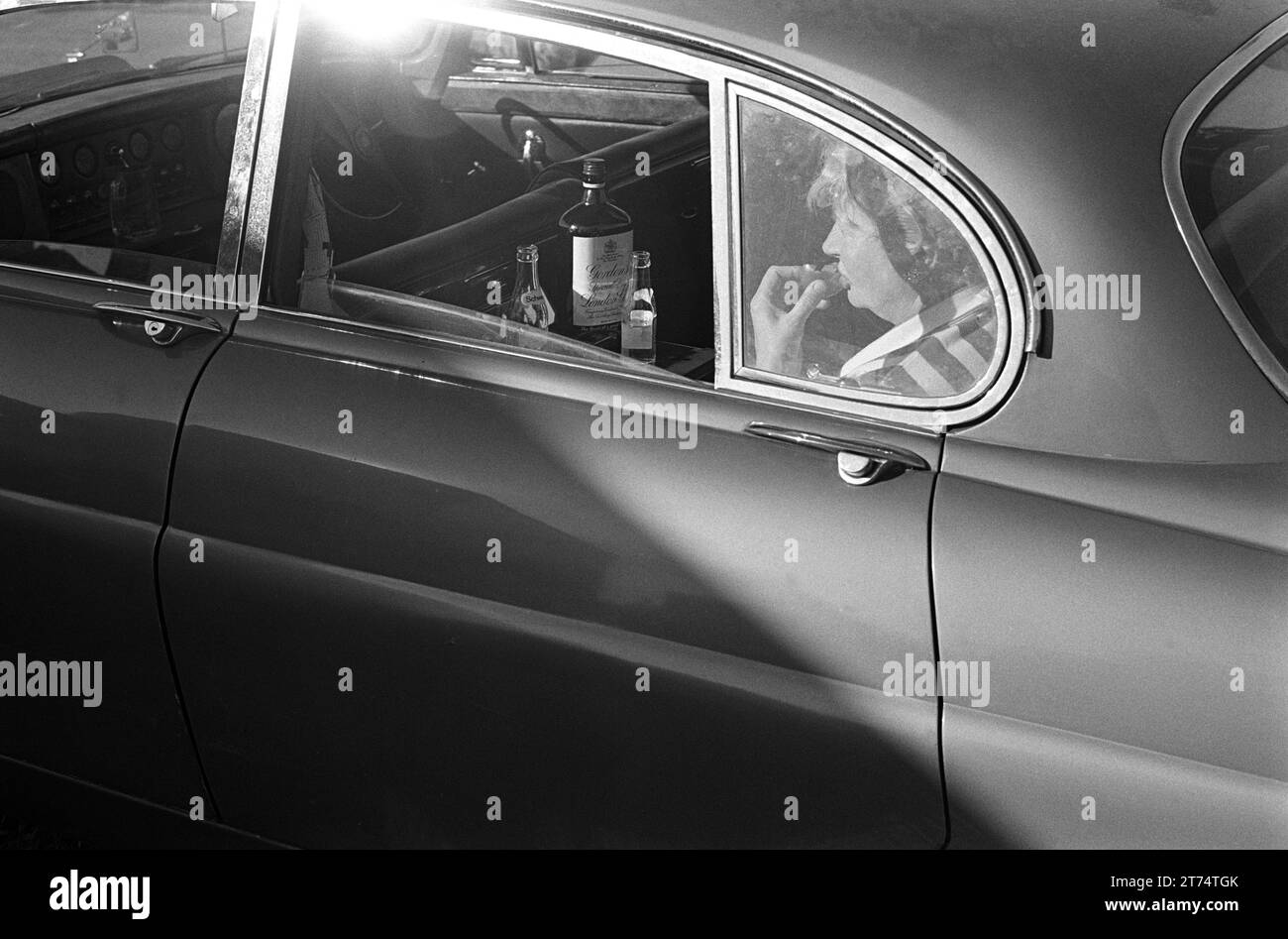 1970s Derby Day UK.  In the car park and before the Off, a racegoer enjoys a Gordon's Special Dry London Gin and tonic and a cup cake in the back of the Jaguar. Epsom Downs, Surrey, England 3rd June 1970.  HOMER SYKES. Stock Photo