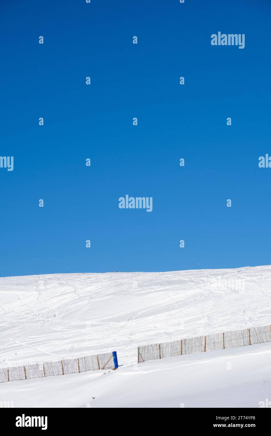 Minimalist landscape on a snowy mountain with a fence with blue sky Stock Photo