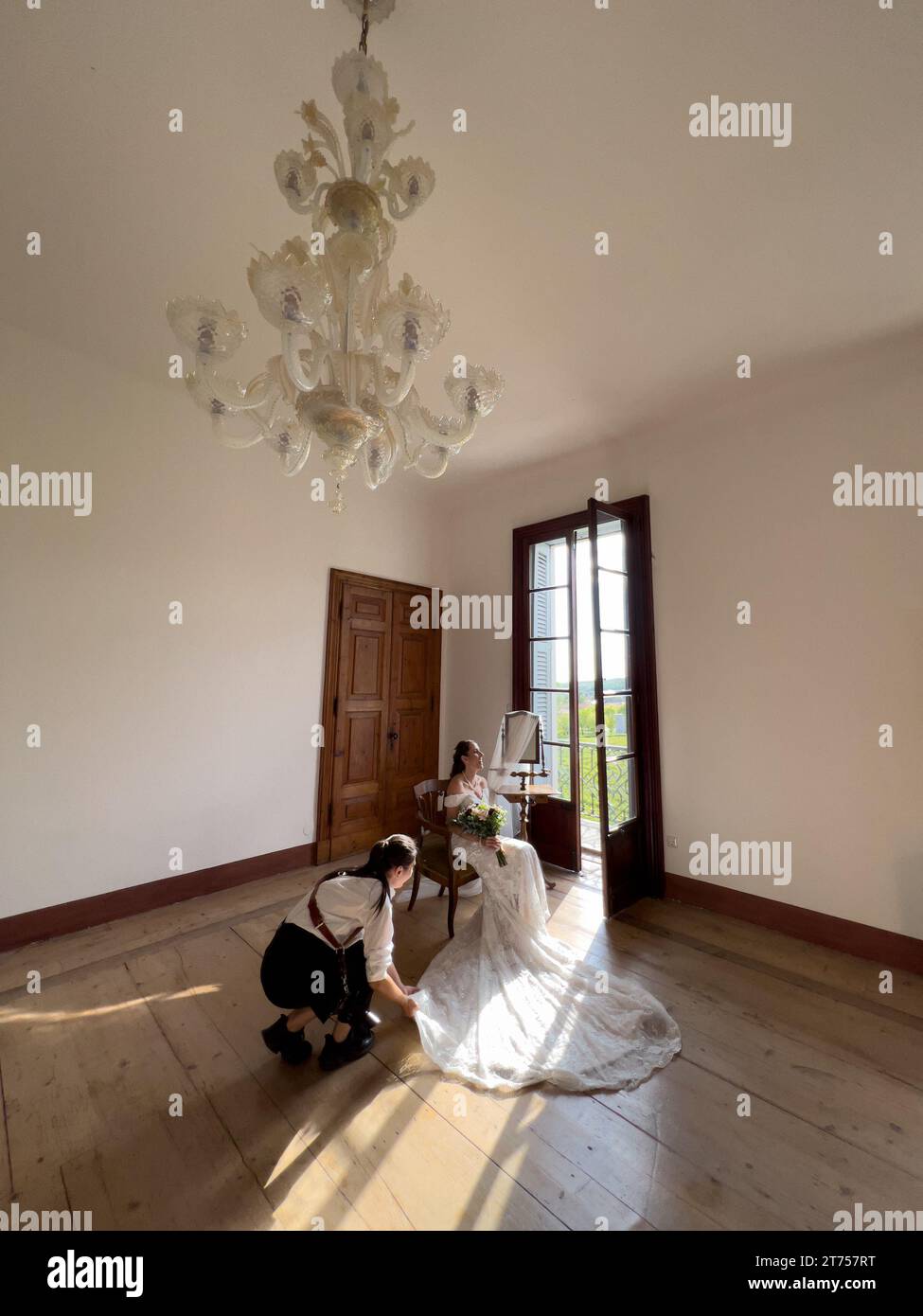 Rome, Italy - 09 august 2023: Girl-photographer adjusts the long train of the wedding dress to the bride sitting on a chair Stock Photo