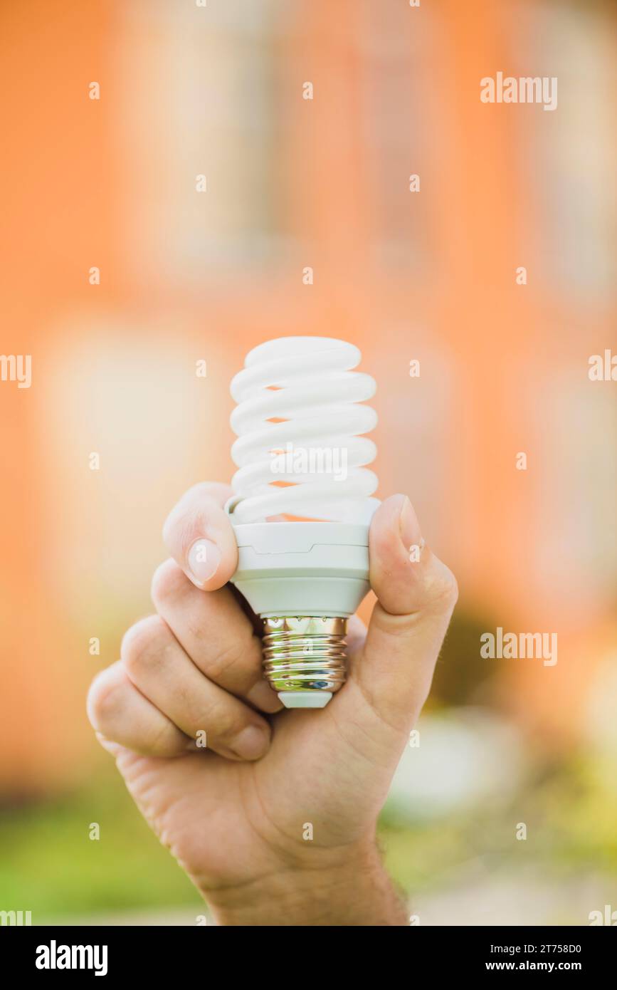 Hand holding energy saving compact fluorescent light bulb outdoors