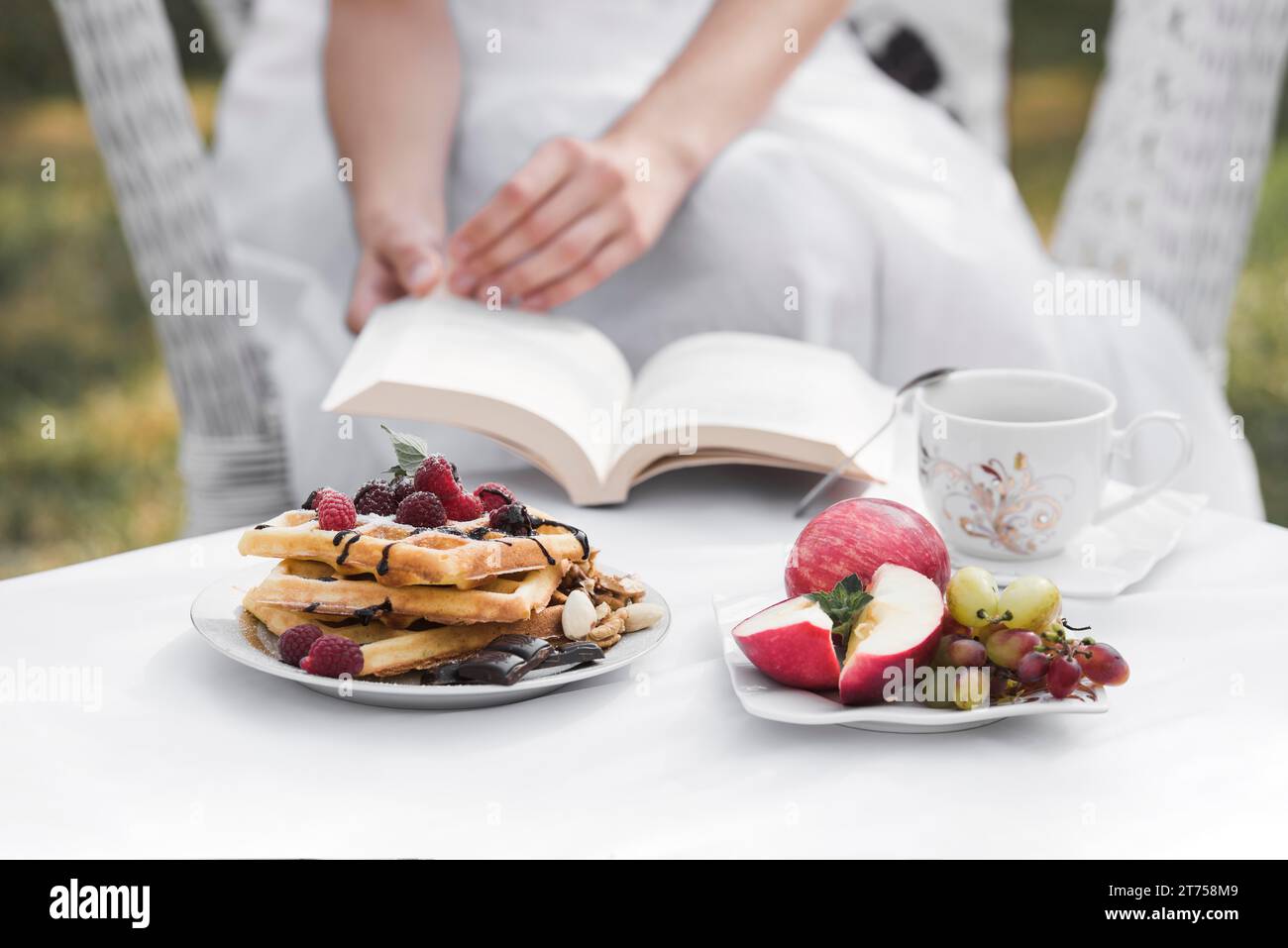 Woman holding book hand with breakfast white table domestic garden Stock Photo