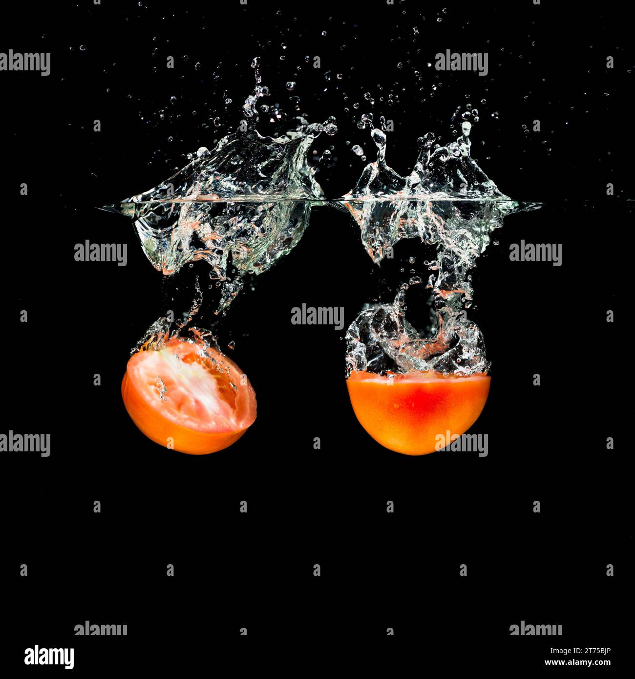 Two halves tomatoes splashing into clean water Stock Photo - Alamy
