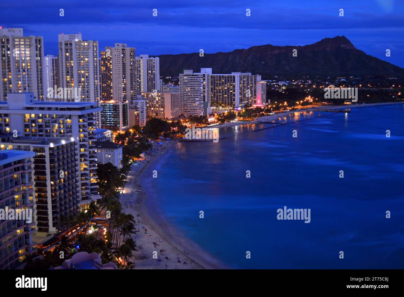 The hotels of Waikiki Beach in Oahu, Hawaii, illuminate along the shore, within view of Diamond Head Mountain Stock Photo