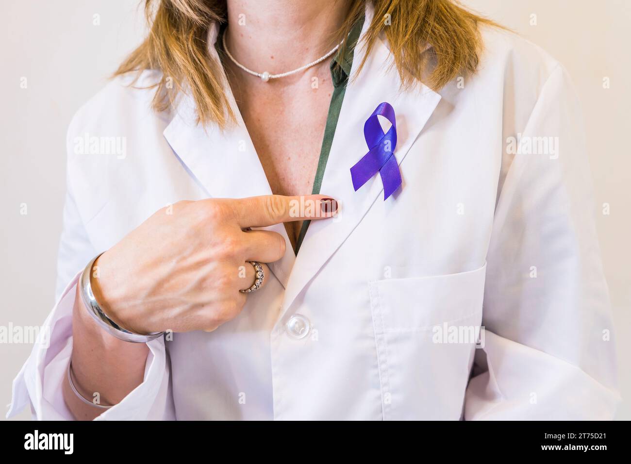 Female doctor wearing a cancer awareness ribbon while pointing at it. Stock Photo