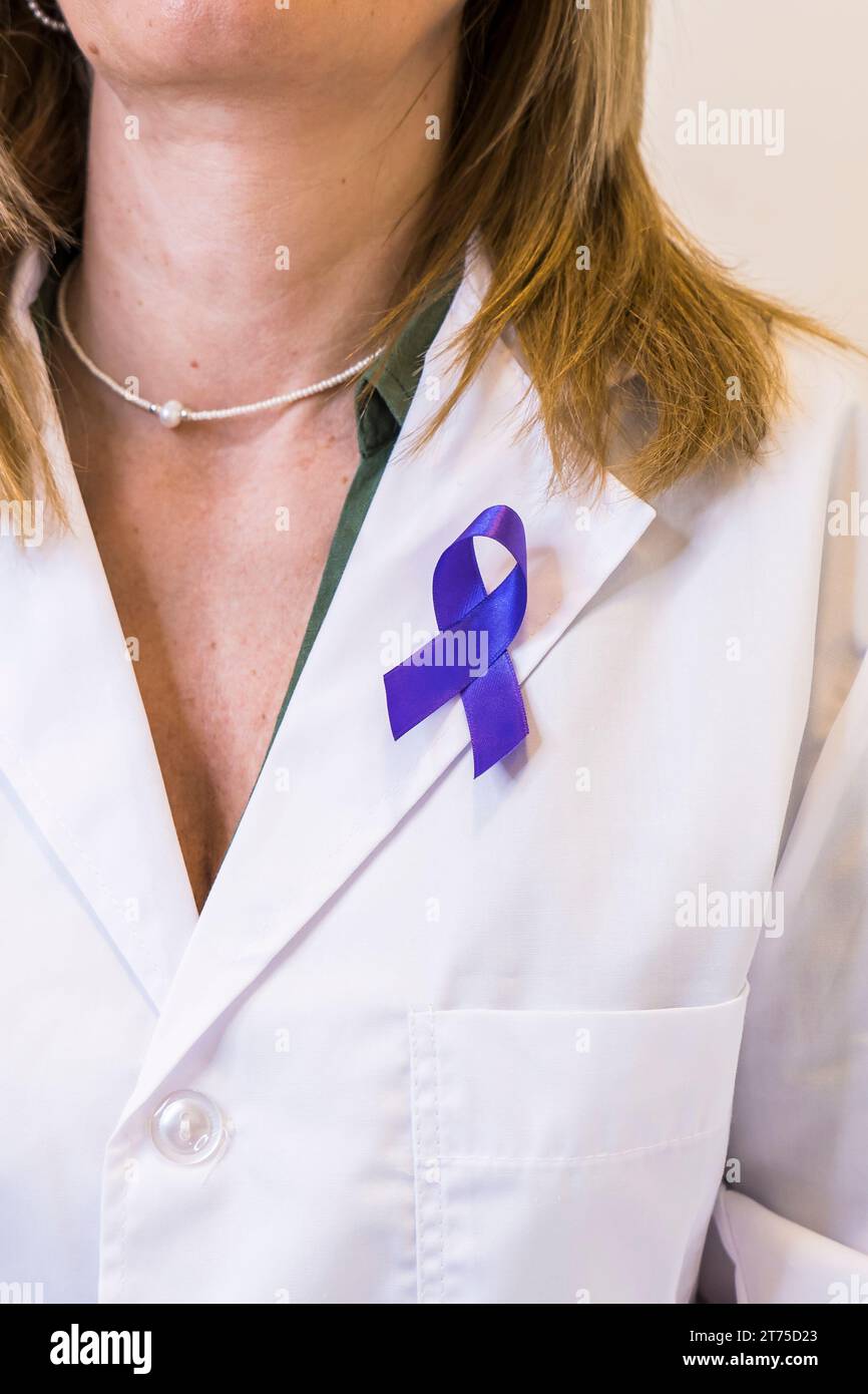 Close-up of purple ribbon pinned on white lab coat of female doctor. Vertical shot Stock Photo