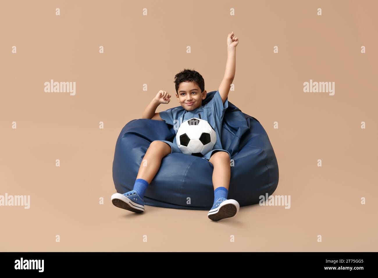 Happy little boy with soccer ball sitting in beanbag chair on beige ...