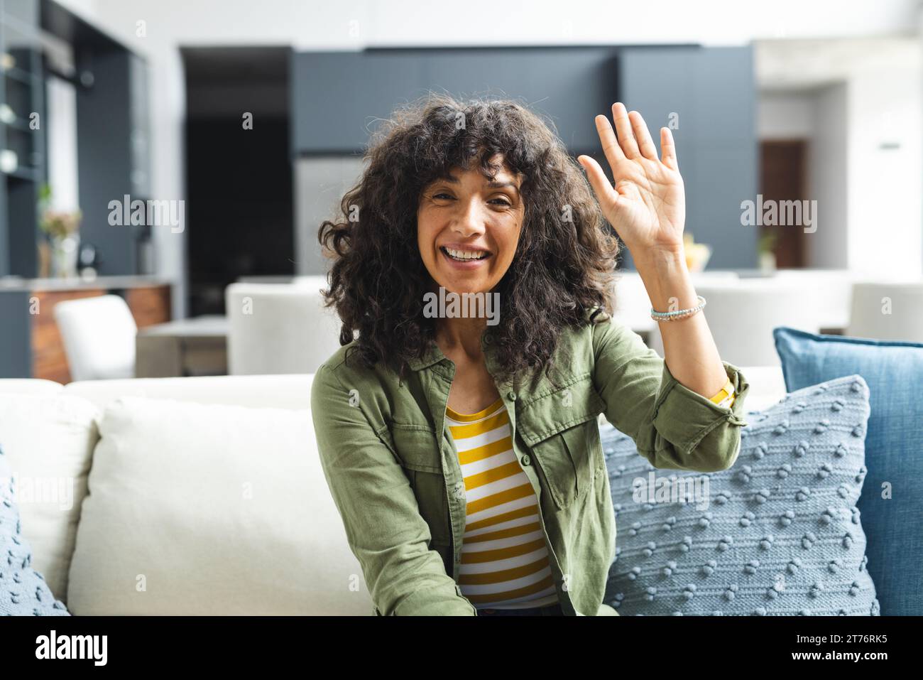 Happy mature caucasian woman having video call, waving on couch in sunny living room, copy space Stock Photo