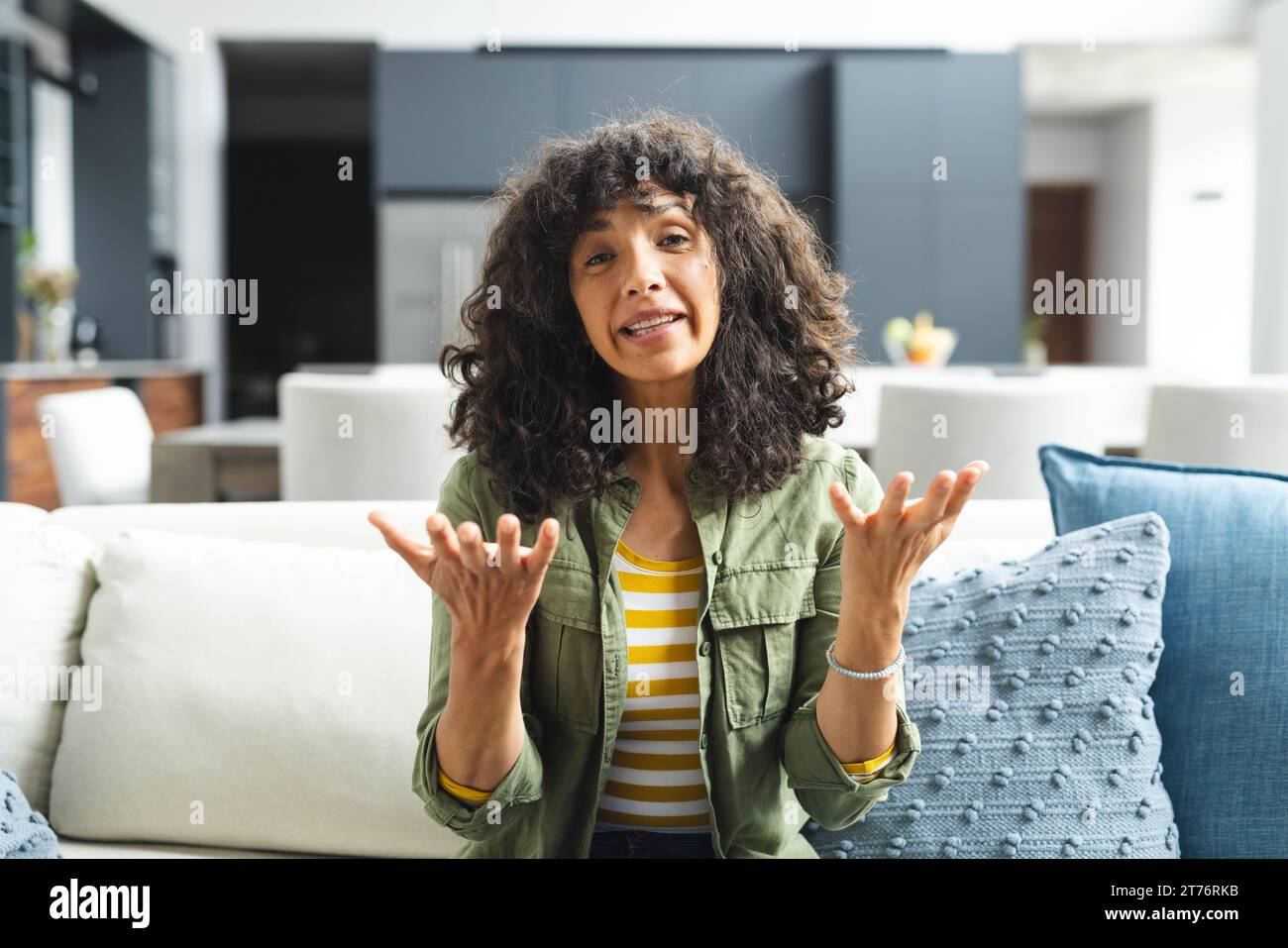 Happy mature caucasian woman having video call, talking and gesturing on couch in sunny living room Stock Photo