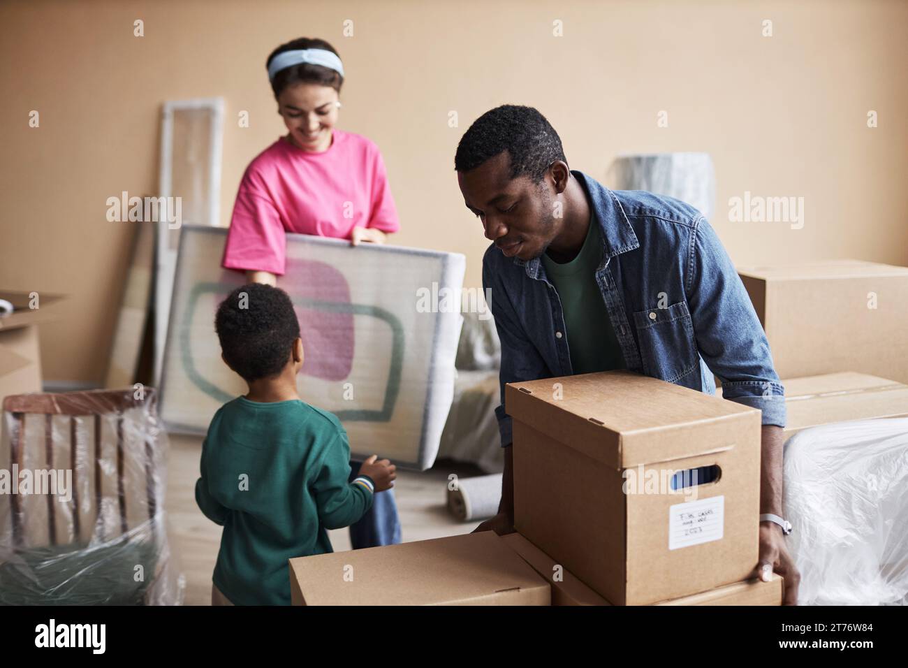 Young African American man putting packed cardboard box with household stuff on top of another one during family relocation Stock Photo
