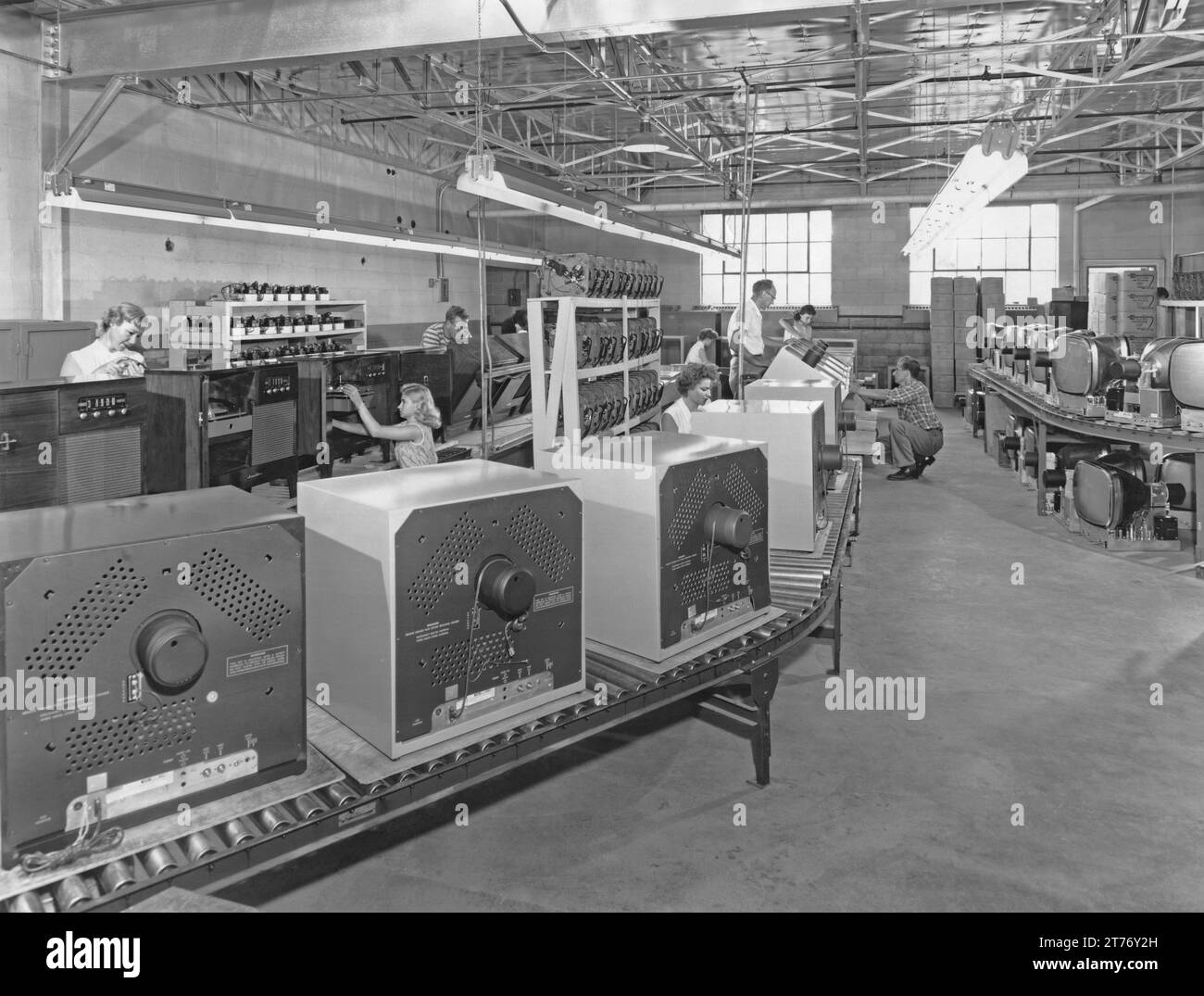 Workers on the production line at a manufacturer of home-entertainment electrical goods in the USA c.1960. The central conveyor has televisions being assembled (unusually housed in a metal casing). The monitor screens (CRTs) that are assembled into the outer units of the TVs are on the right. On the left the production line is turning out radiograms or consoles, wooden units with legs. The record player/changer units are stacked next to the line. In the far right boxes in the corner indicate that these components were supplied by V-M (‘Voice of Music’) of Benton Harbor, Michigan. Stock Photo
