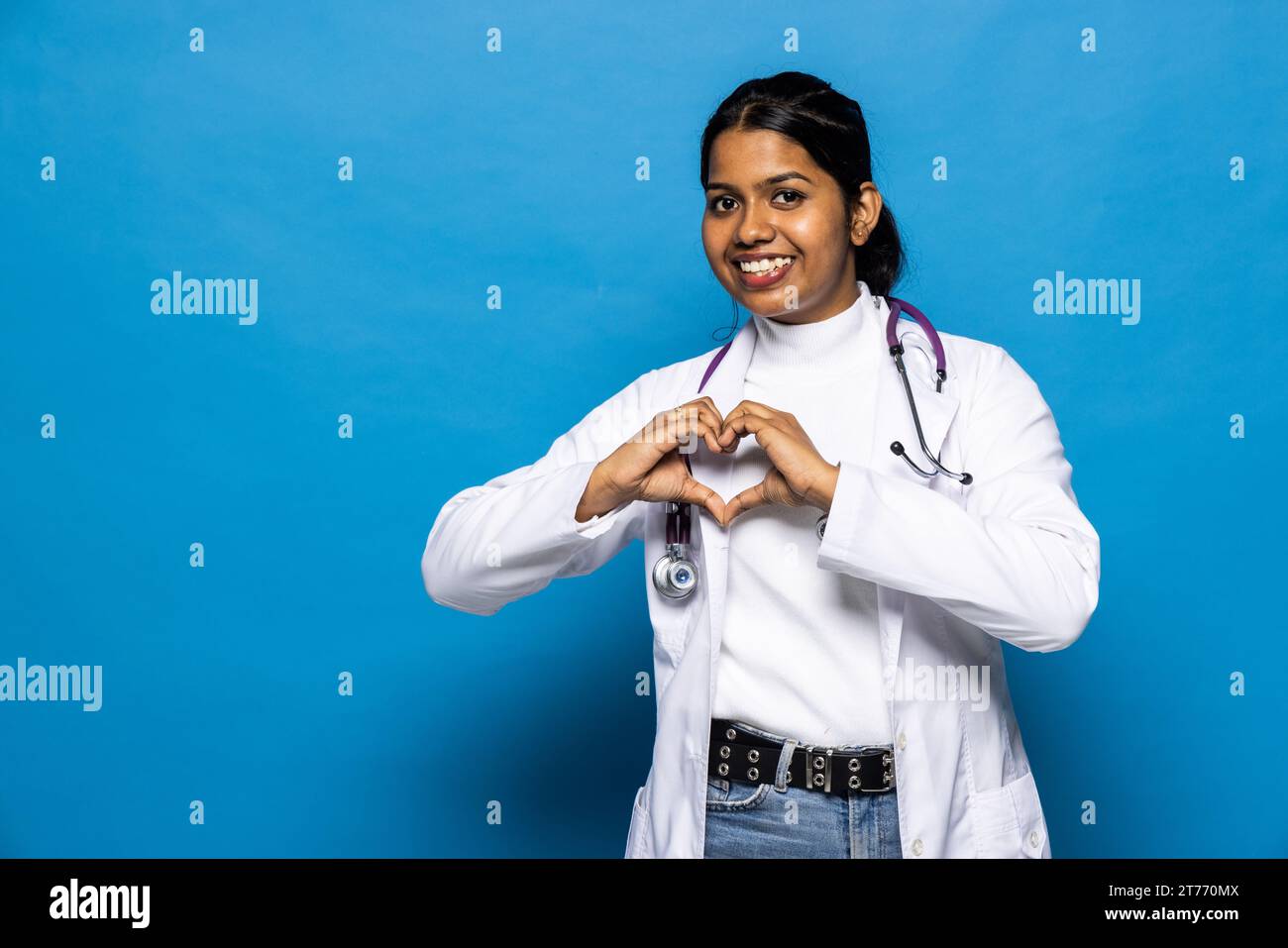 Smiling pretty young indian woman doctor in coat with stethoscope makes ...