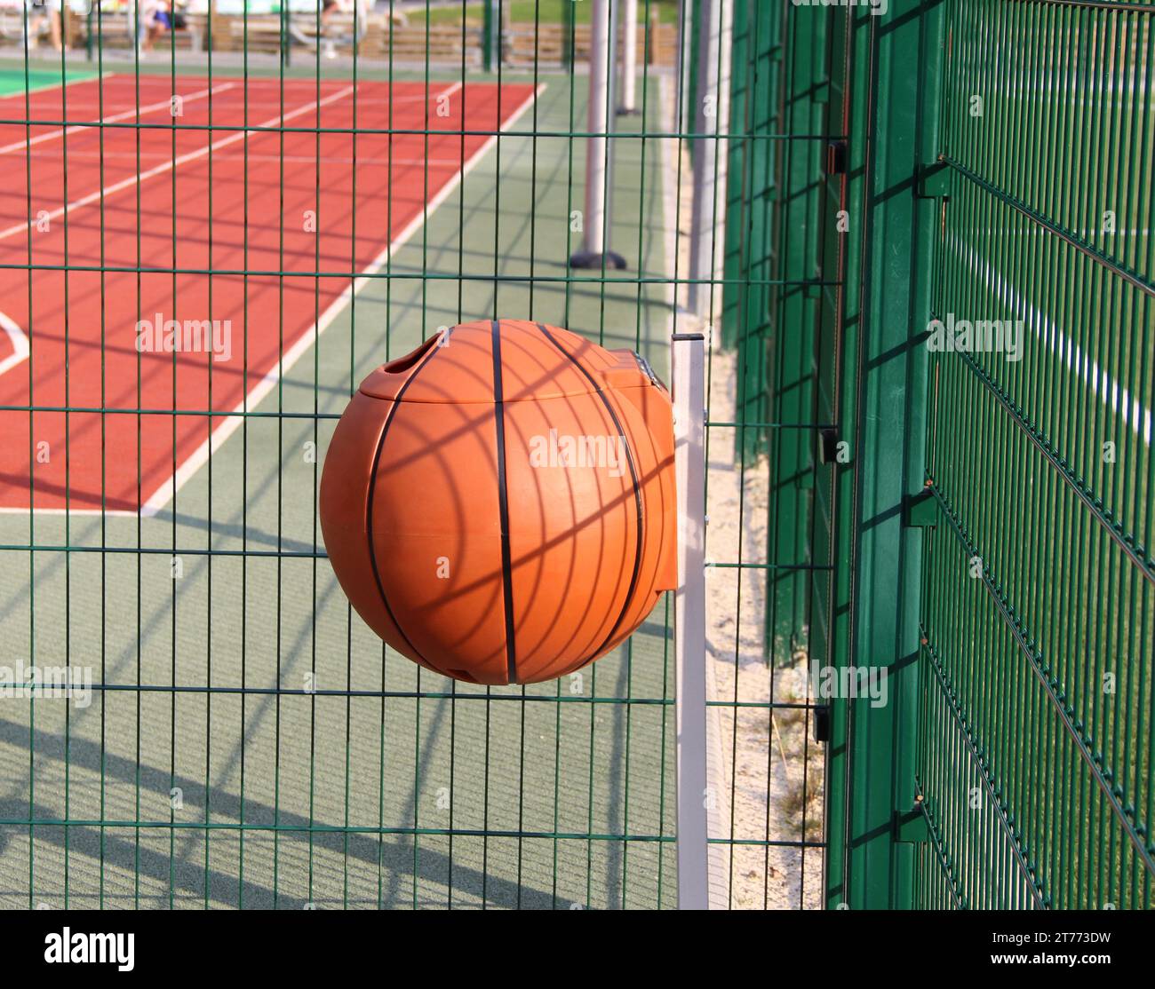 Round trash can in the shape of a basketball ball near fenced basketball court Stock Photo Alamy