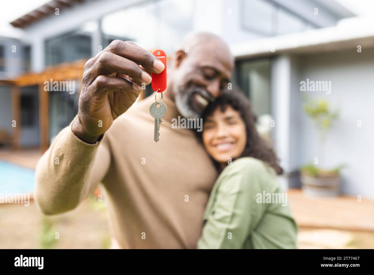 Happy diverse couple holding house keys embracing outside new home ...