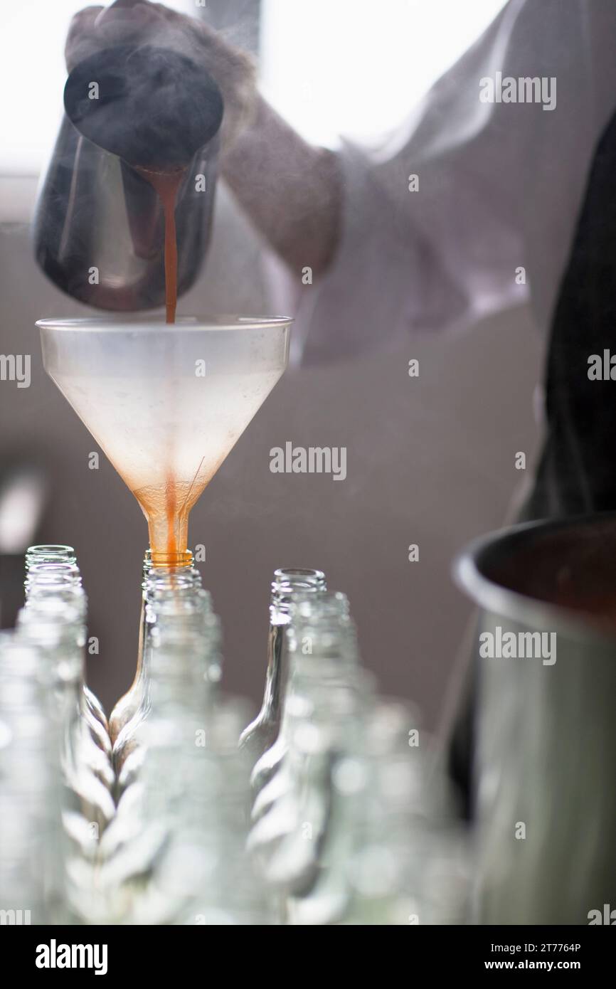 Factory worker pouring tomato sauce through a funnel into bottles