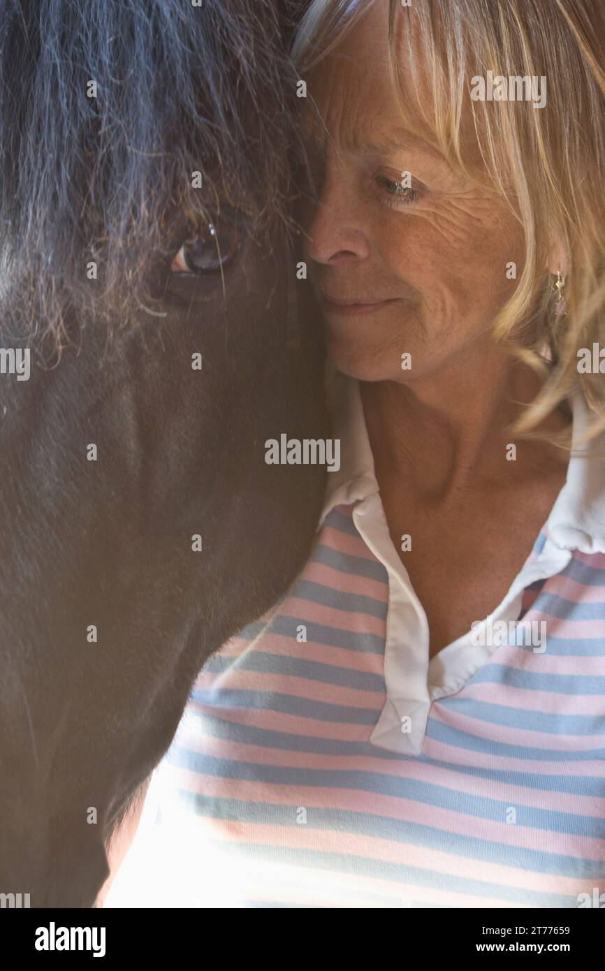 Close up of a mature woman standing next to horse head Stock Photo