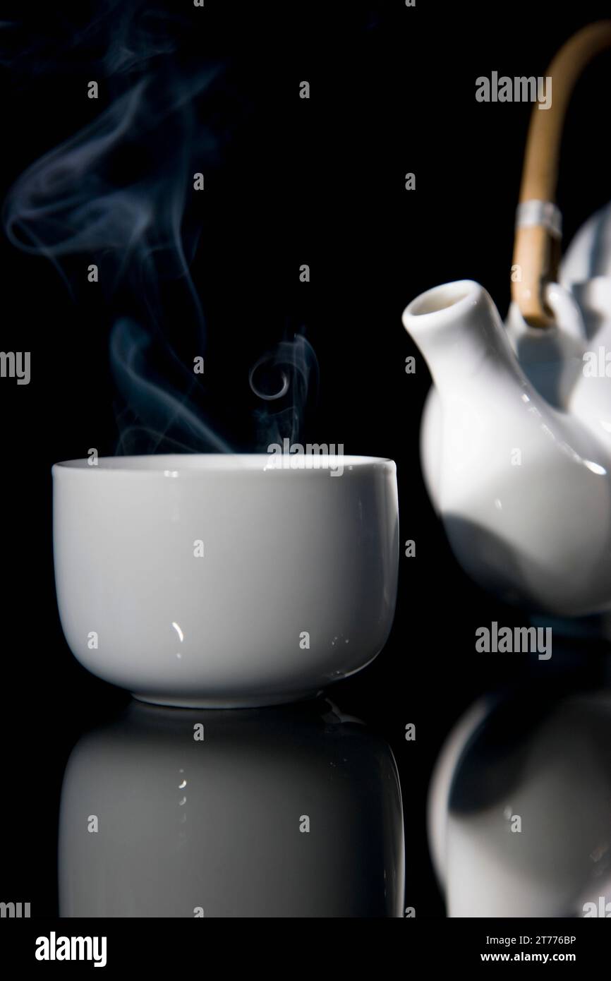 Close up of a steaming green tea teacup and detail of a teapot with wooden handle Stock Photo